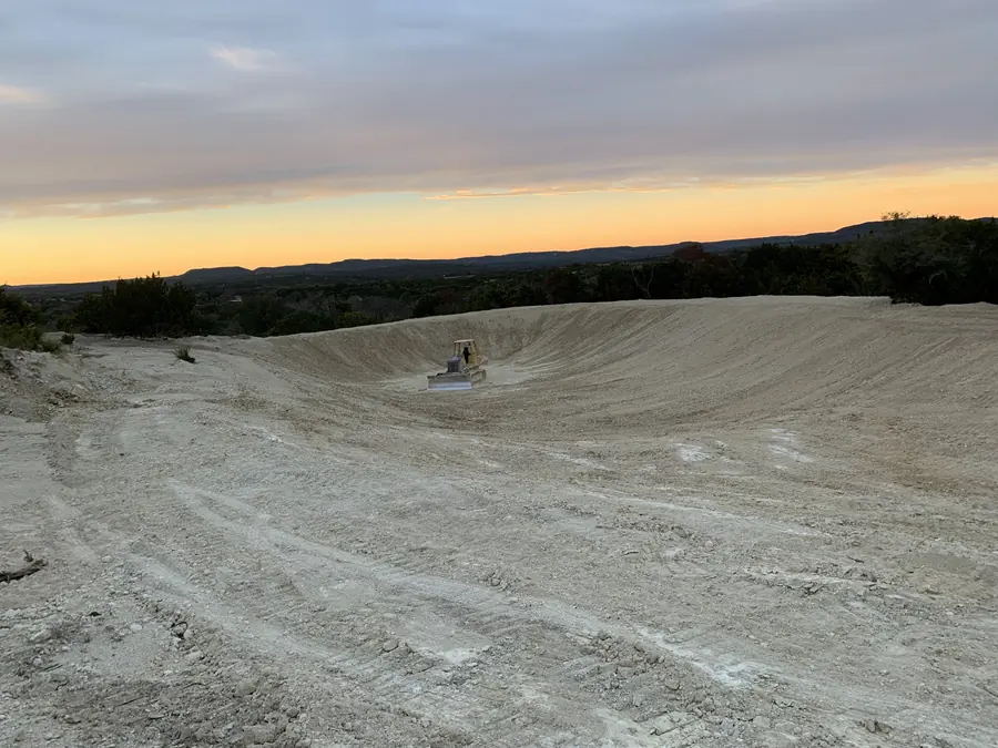 Large earthen tank basin at dusk with a dozer small on the floor of the dig