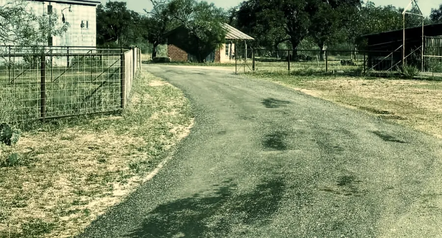 Finished driveway curving past a pipe and wire ranch gate