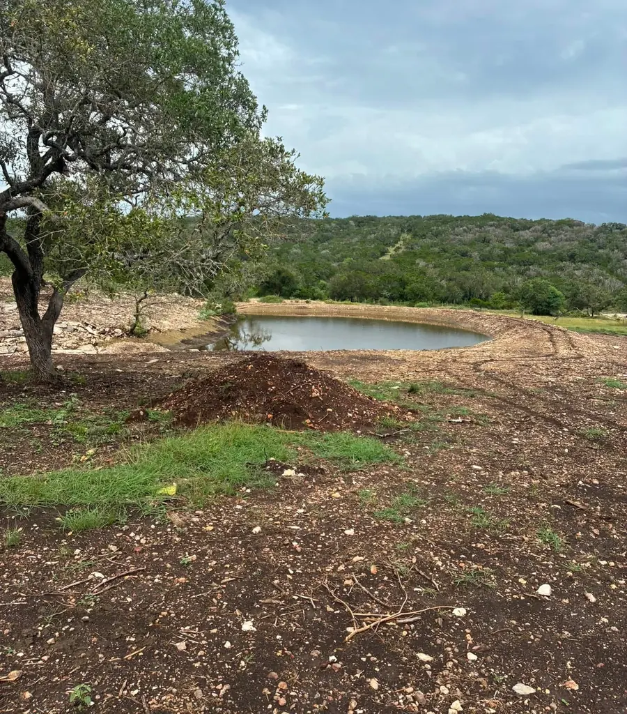New stock pond with a spoil berm, an oak tree in front and wooded hills behind